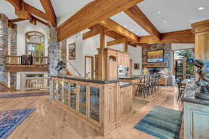 Kitchen featuring a stone fireplace, light wood finished floors, light brown cabinetry, beamed ceiling, and high vaulted ceiling