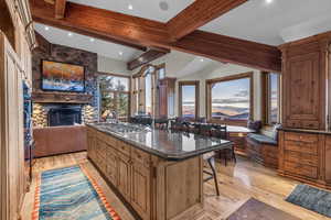 Kitchen featuring a kitchen breakfast bar, dark stone countertops, light wood finished floors, brown cabinets, and beam ceiling