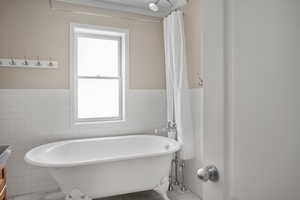 Full bath with tile walls, tile patterned floors, healthy amount of natural light, a freestanding bath, and wainscoting
