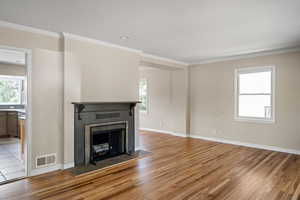 Unfurnished living room featuring light wood-style flooring, healthy amount of natural light, a tiled fireplace, and crown molding
