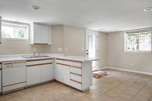 Kitchen with dishwasher, a sink, a peninsula, light countertops, and white cabinets
