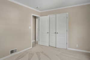 Unfurnished bedroom with light colored carpet, crown molding, baseboards, and a closet