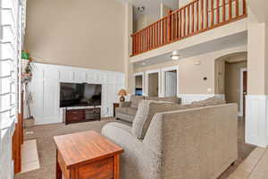 Living room featuring arched walkways, a towering ceiling, wainscoting, light tile patterned flooring, and a decorative wall