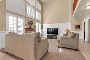 Living room with a high ceiling, light tile patterned floors, a fireplace, a decorative wall, and plenty of natural light