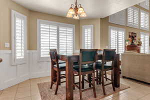 Dining area with light tile patterned floors, plenty of natural light, a chandelier, a wainscoted wall, and a decorative wall