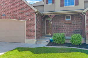 Entrance to property featuring brick siding, an attached garage, driveway, and stucco siding