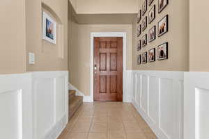 Foyer with light tile patterned flooring, a wainscoted wall, and stairway