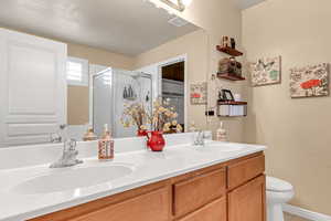 Bathroom with double vanity, a shower stall, toilet, and tile patterned floors
