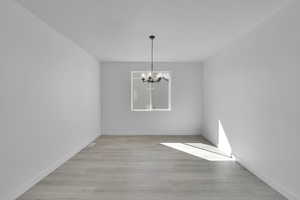 Unfurnished dining area featuring a chandelier, light wood-style flooring, and baseboards