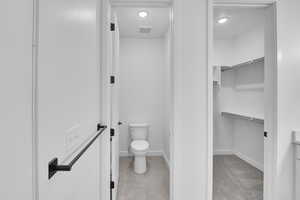 Bathroom with toilet, recessed lighting, a walk in closet, baseboards, and tile patterned floors