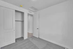 Unfurnished bedroom featuring carpet floors, attic access, baseboards, and a closet
