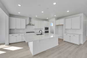 Kitchen featuring wall chimney exhaust hood, a sink, appliances with stainless steel finishes, an island with sink, and decorative backsplash