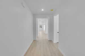 Hallway featuring light wood finished floors, baseboards, and recessed lighting