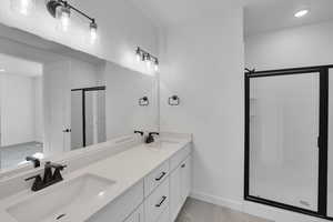 Bathroom with a shower stall, double vanity, baseboards, recessed lighting, and tile patterned flooring