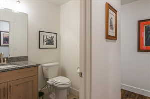 Half bathroom with toilet, vanity, wood finished floors, and baseboards