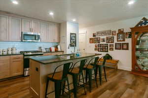 Kitchen with appliances with stainless steel finishes, a sink, dark countertops, dark wood-style flooring, and decorative backsplash