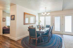 Dining room with a chandelier, a textured ceiling, baseboards, and dark wood-style flooring