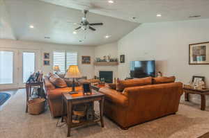 Carpeted living room with vaulted ceiling, recessed lighting, ceiling fan, and a glass covered fireplace