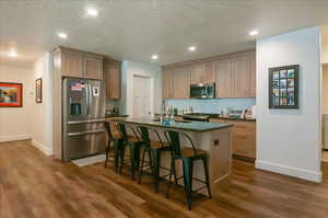Kitchen featuring appliances with stainless steel finishes, dark countertops, a sink, dark wood-style flooring, and baseboards