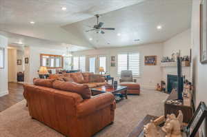 Living room with vaulted ceiling, a textured ceiling, baseboards, a ceiling fan, and a tile fireplace