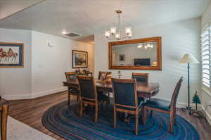 Dining area with a chandelier, dark wood-style floors, baseboards, and a textured ceiling