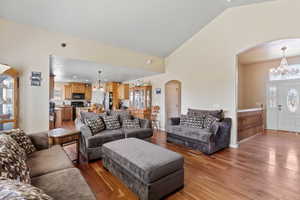 Living area with arched walkways, a chandelier, light wood-style flooring, and high vaulted ceiling