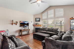 Living area with ceiling fan, high vaulted ceiling, a glass covered fireplace, light wood-type flooring, and baseboards
