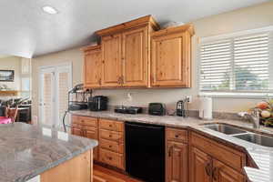 Kitchen with dishwasher, a sink, a textured ceiling, light wood-type flooring, and light stone counters