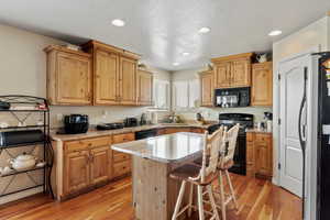 Kitchen with black appliances, a sink, light wood-type flooring, a kitchen island, and a textured ceiling