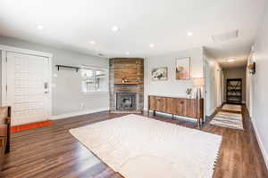 Living room featuring baseboards, dark wood-type flooring, recessed lighting, and a stone fireplace