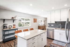 Kitchen featuring stainless steel appliances, a sink, dark wood finished floors, a kitchen island, and white cabinetry