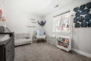 Carpeted bedroom featuring a crib and baseboards