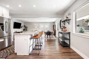 Kitchen featuring stainless steel fridge, a breakfast bar area, white cabinets, dark wood-type flooring, and recessed lighting