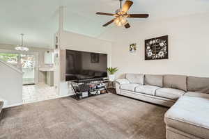 Living room with carpet flooring, a ceiling fan, lofted ceiling, baseboards, and a chandelier