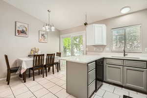 Kitchen with gray cabinets, a peninsula, a sink, lofted ceiling, and light countertops