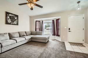 Carpeted living area featuring lofted ceiling, a ceiling fan, baseboards, and tile patterned floors