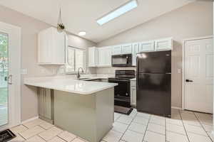 Kitchen featuring black appliances, a sink, a peninsula, vaulted ceiling, and light countertops