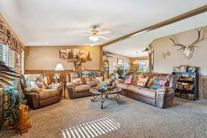 Carpeted living area with a chandelier, ceiling fan, and a wainscoted wall