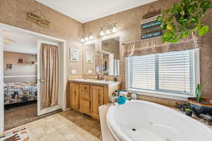 Ensuite bathroom with a tub with jets, double vanity, a textured wall, and stone finish floors