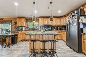 Kitchen featuring stainless steel fridge with ice dispenser, electric range oven, under cabinet range hood, a center island, and a kitchen breakfast bar
