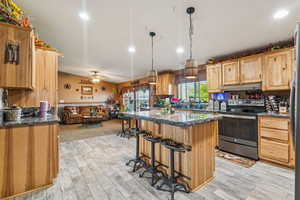 Kitchen with electric range, under cabinet range hood, open floor plan, a kitchen breakfast bar, and a kitchen island