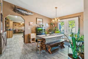 Dining space featuring light wood-type flooring, a chandelier, french doors, and baseboards