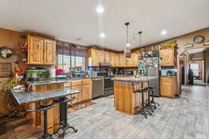 Kitchen with stainless steel appliances, a breakfast bar area, under cabinet range hood, light wood-type flooring, and recessed lighting
