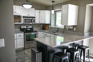 Kitchen featuring stainless steel appliances, a peninsula, a sink, white cabinetry, and a breakfast bar area