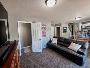 Living room featuring carpet flooring, stairway, a textured ceiling, and baseboards