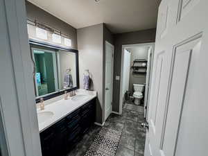 Bathroom featuring double vanity, toilet, a textured ceiling, and baseboards