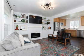 Living area with a chandelier, healthy amount of natural light, a glass covered fireplace, and dark wood-style flooring
