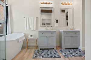 Bathroom featuring wood finished floors, two vanities, baseboards, and a freestanding tub
