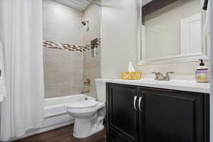 Bathroom with shower / bathtub combination with curtain, vanity, wood finished floors, and toilet