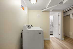 Washroom featuring washer and dryer, light wood-style floors, a textured ceiling, and baseboards
